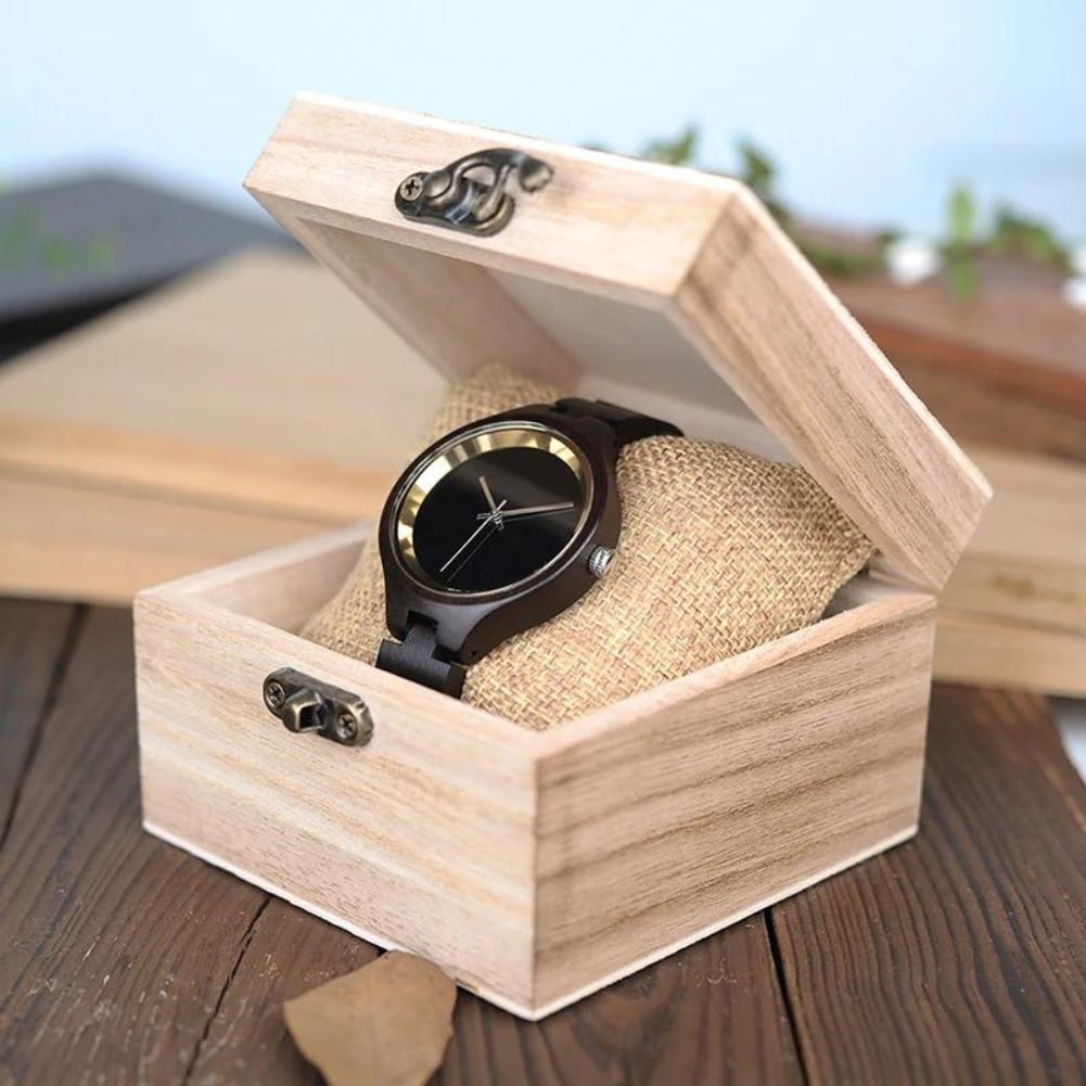 Die Holzuhr Luna liegt in einer Holzbox auf einem Holztisch. Der Hintergrund zeigt möglicherweise Holzbretter oder eine Holzstruktur.